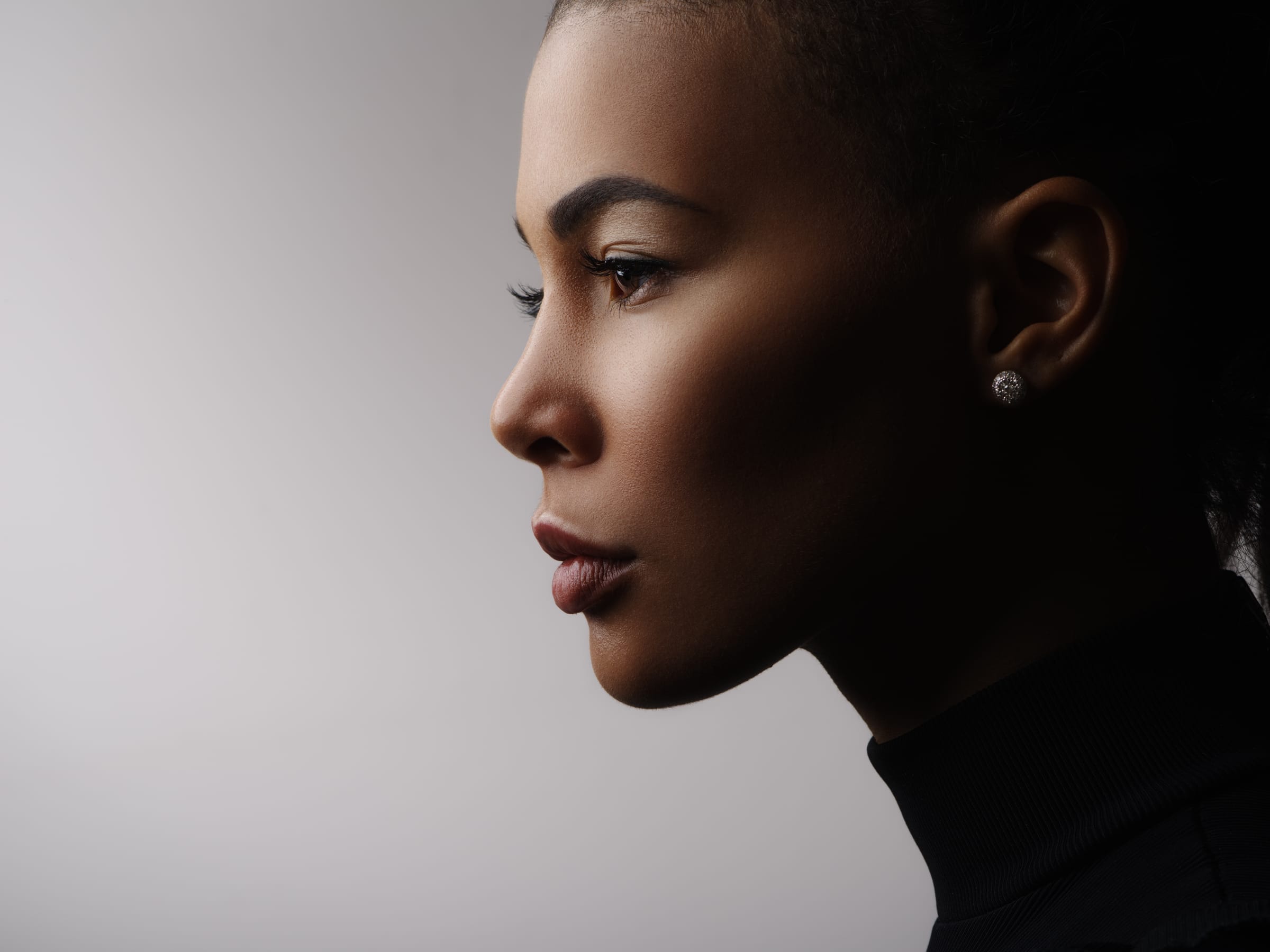 A model in profile against a soft grey studio background, her face lit from the side