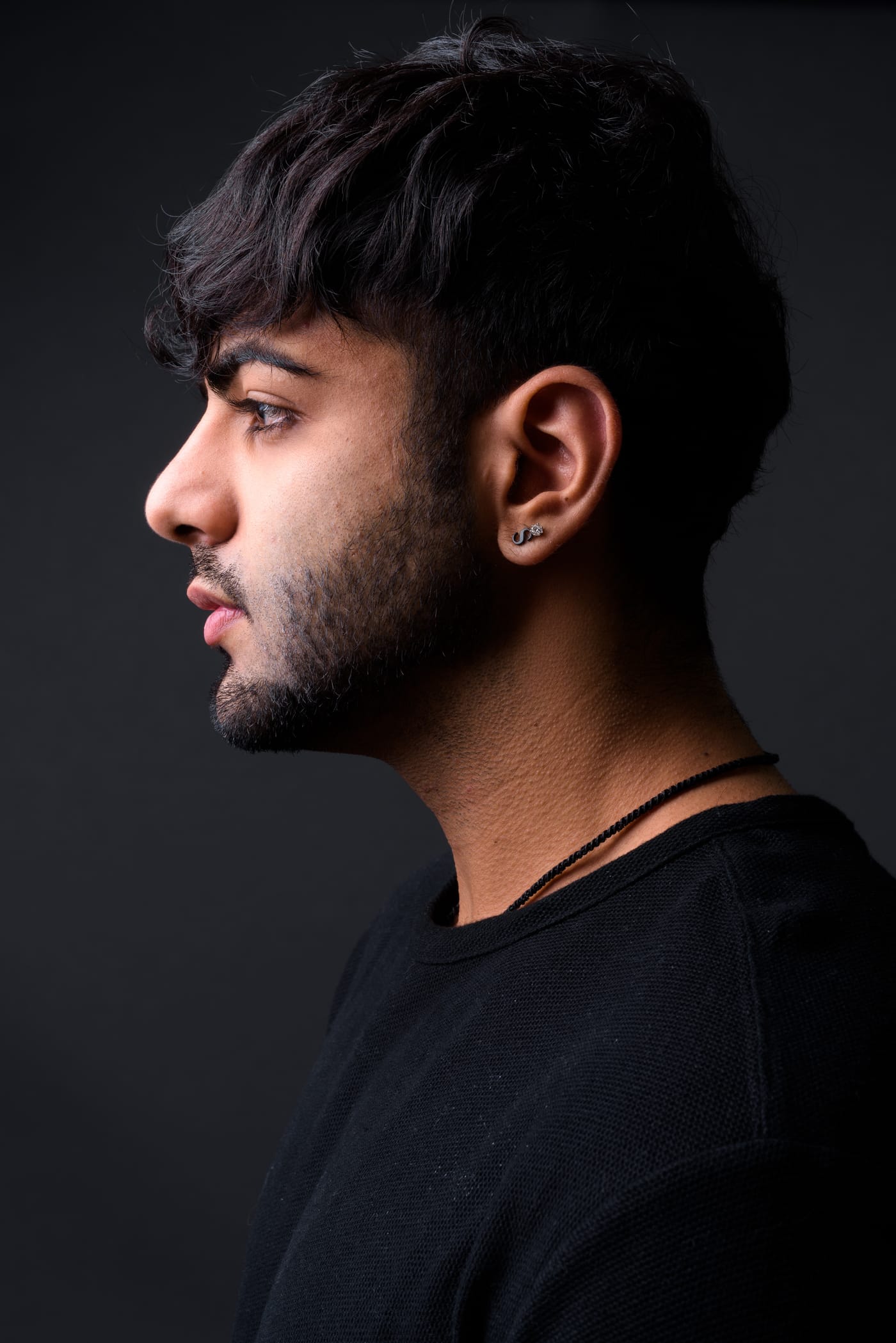 A male model in profile in a black T-shirt against a dark grey background