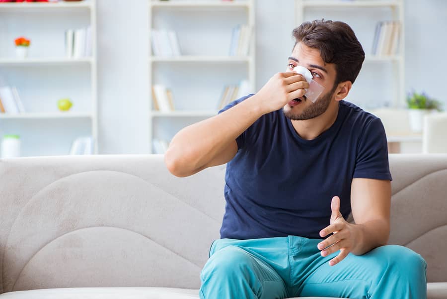 A man seated on a sofa holding a tissue to his nose