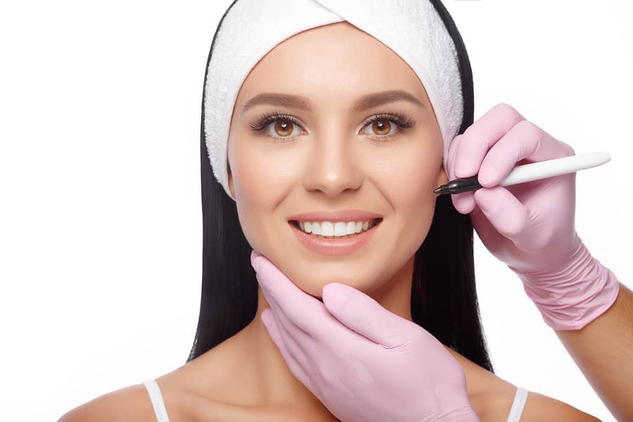 A smiling woman in a headband while gloved hands hold a marking pen near her face