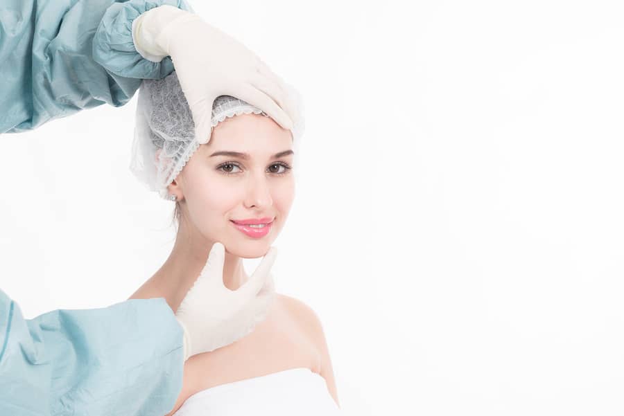 A woman in a surgical cap with gloved hands framing her face