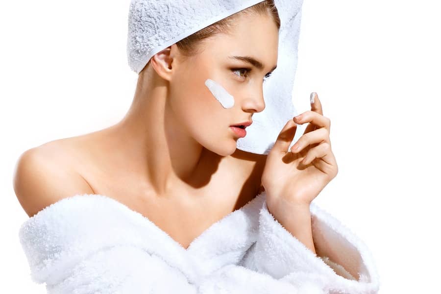A woman in a bathrobe and towel wrap with a dab of cream on her cheek
